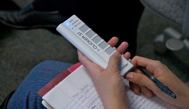 A student uses an iclicker while writing notes.