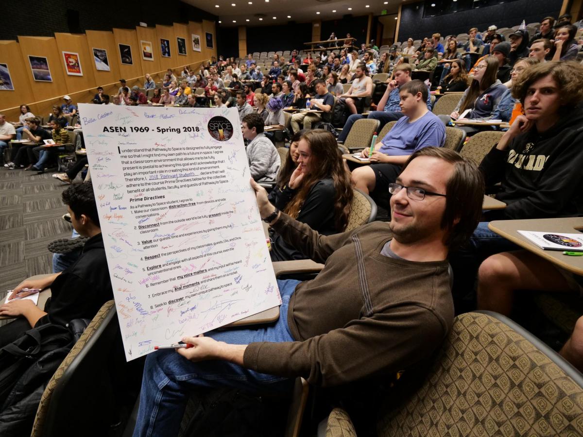 student holding up poster size prime directives