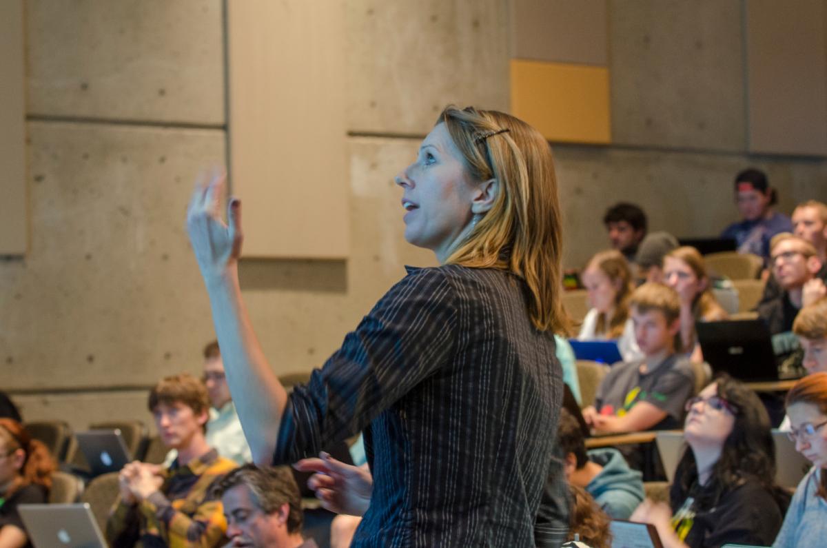 Instructor looks toward a screen while teaching in a large classroom.