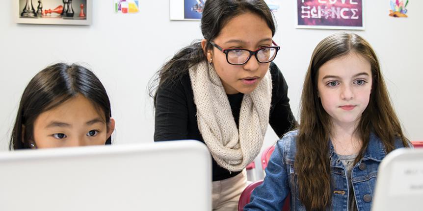A woman helps two girls at a Girls Who Code club.