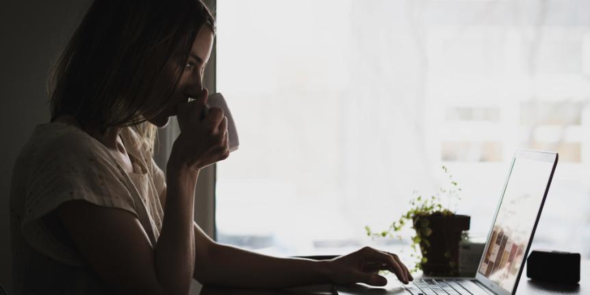 Sipping coffee and looking at laptop computer.