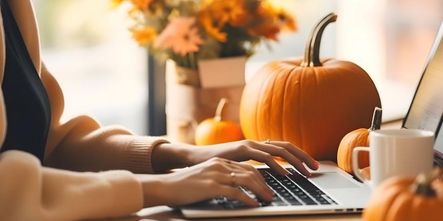 Someone using a computer on a desktop with decorative pumpkins.