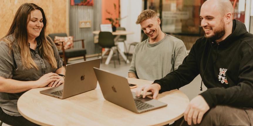 Three people sitting at a table with mac laptops