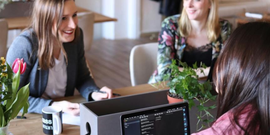 Three women sitting at a table smiling with laptops