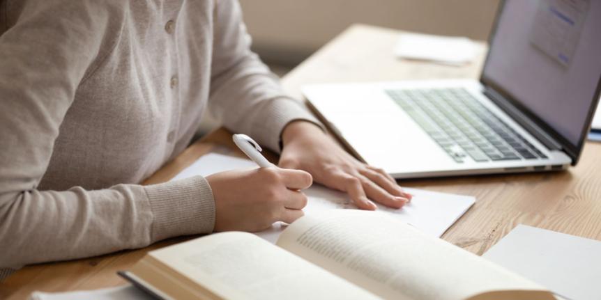 Someone taking notes with a computer in the background