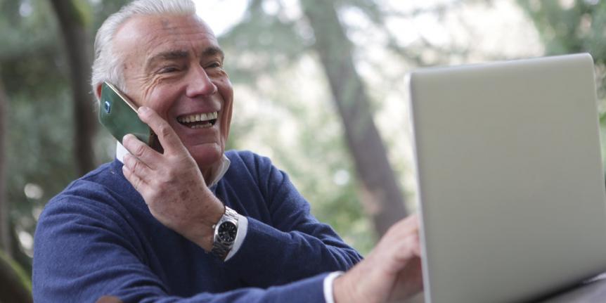 Retiree speaking on phone while looking at laptop.
