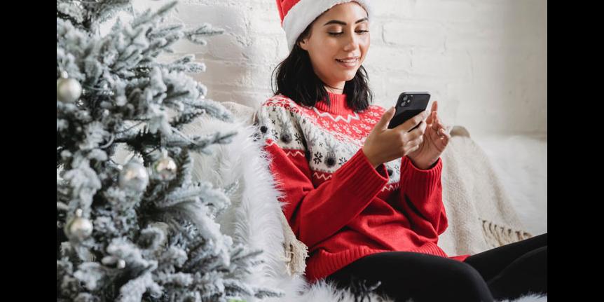 Decorative photo: woman looking at phone with Christmas tree nearby