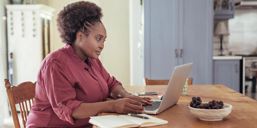 Decorative photo: a woman uses her laptop on a dining table in her home.