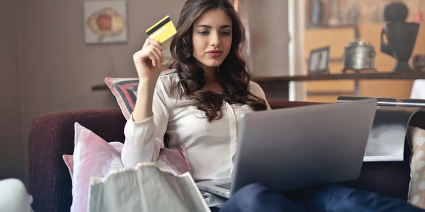 Decorative photo: young woman looks at her laptop while holding a credit card.
